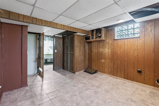 basement with a drop ceiling, wooden walls, and tile patterned flooring