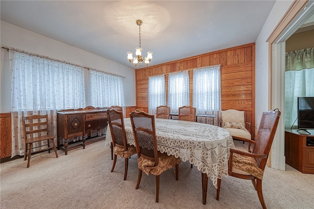 dining space with wood walls, a chandelier, and light carpet