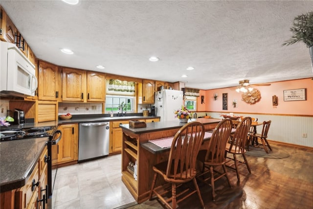 kitchen featuring a center island, a textured ceiling, light tile patterned floors, white appliances, and ceiling fan