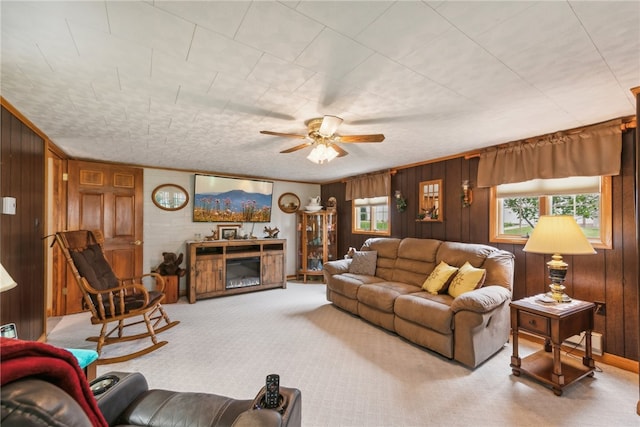 carpeted living room featuring wood walls, ornamental molding, ceiling fan, and a fireplace