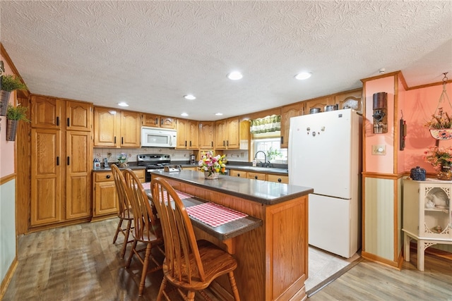 kitchen featuring a kitchen island, a kitchen bar, light hardwood / wood-style floors, a textured ceiling, and white appliances