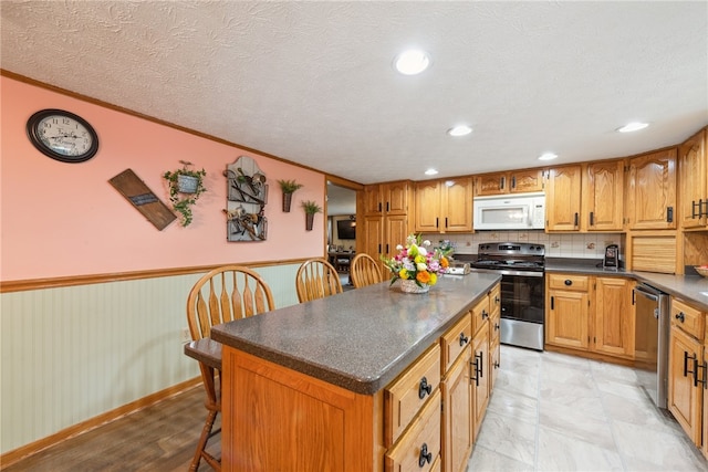 kitchen with backsplash, ornamental molding, a textured ceiling, a center island, and stainless steel appliances