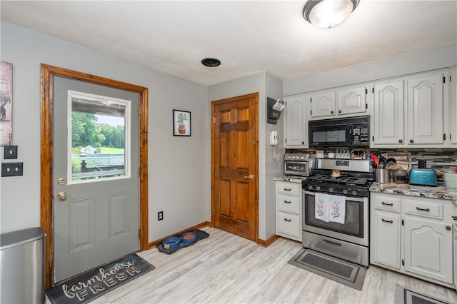 kitchen featuring light wood-type flooring, white cabinets, stainless steel gas stove, and tasteful backsplash