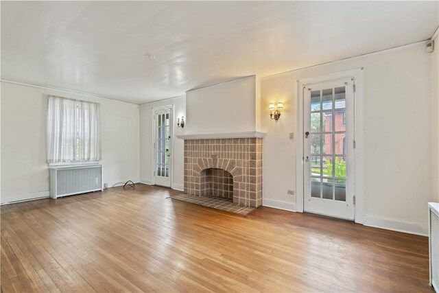 unfurnished living room with light hardwood / wood-style flooring, radiator heating unit, and a tiled fireplace