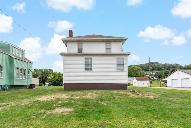 back of house featuring a garage, a yard, cooling unit, and an outbuilding