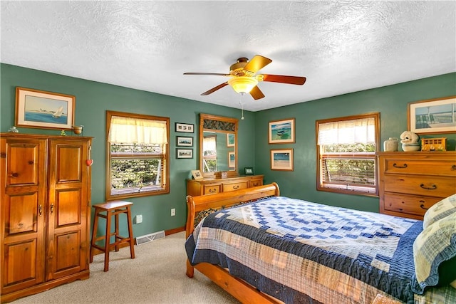 bedroom with a textured ceiling, light colored carpet, visible vents, and baseboards