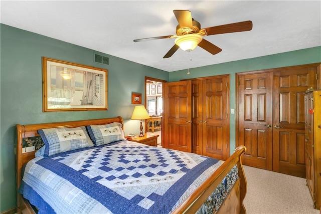 carpeted bedroom featuring visible vents, two closets, and a ceiling fan