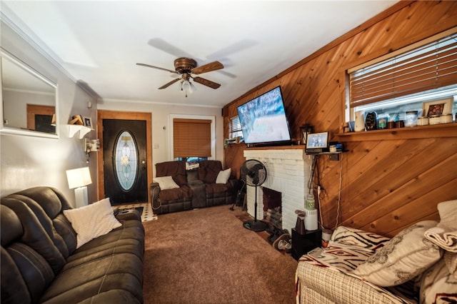 carpeted living room featuring ceiling fan, wooden walls, ornamental molding, and a brick fireplace