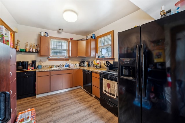 kitchen with sink, black appliances, light stone counters, and light hardwood / wood-style flooring