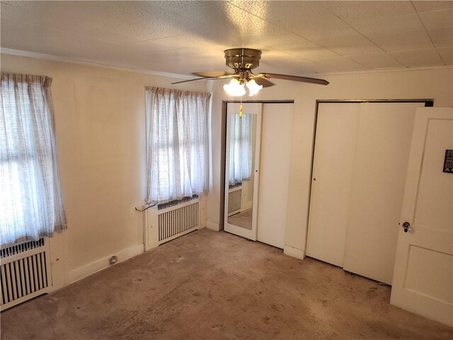 unfurnished bedroom featuring light carpet, two closets, radiator, and ceiling fan