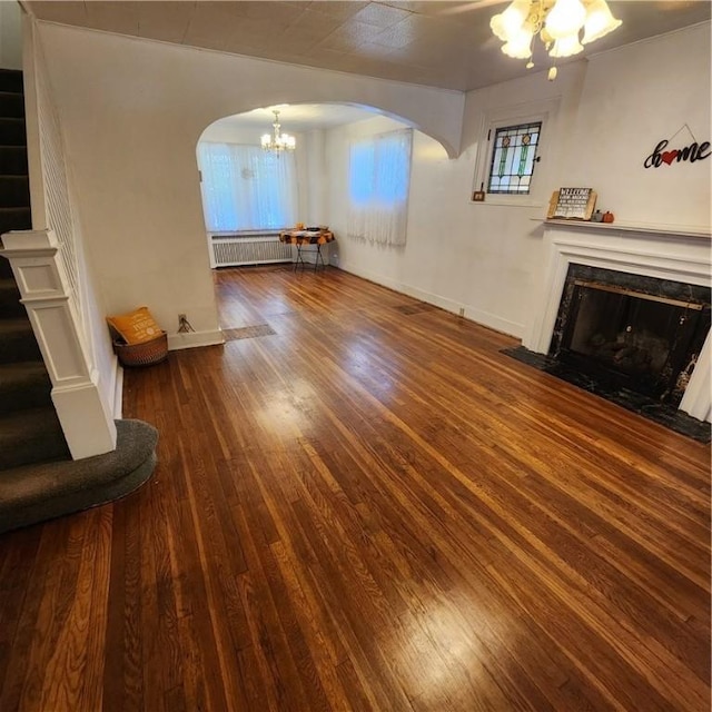 unfurnished living room featuring arched walkways, radiator, a premium fireplace, stairway, and hardwood / wood-style floors