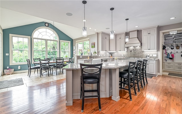 kitchen featuring a kitchen island, light stone counters, light hardwood / wood-style floors, a kitchen bar, and custom range hood