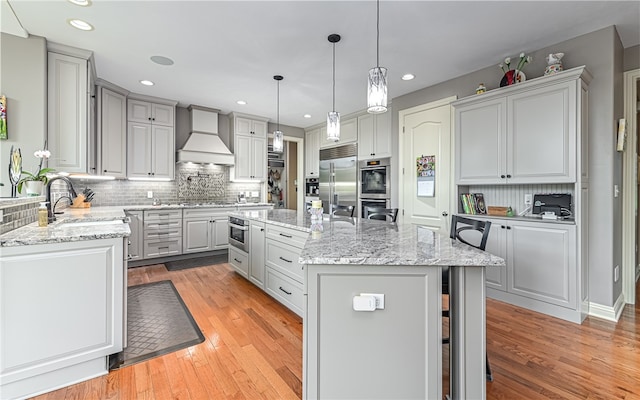 kitchen with premium range hood, sink, a center island, and light hardwood / wood-style flooring