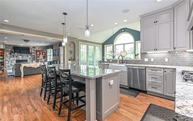 kitchen featuring stainless steel appliances, vaulted ceiling, sink, a stone fireplace, and a breakfast bar area