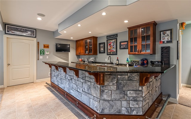 bar with sink, light tile patterned floors, and dark stone counters