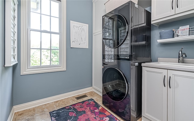 clothes washing area with stacked washer / dryer, sink, and cabinets