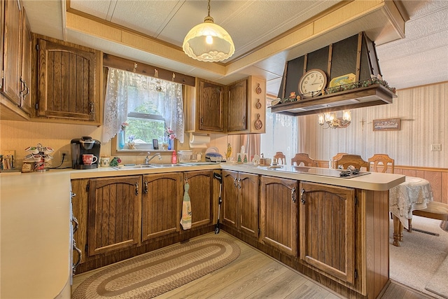 kitchen with black electric cooktop, sink, decorative light fixtures, light hardwood / wood-style flooring, and kitchen peninsula