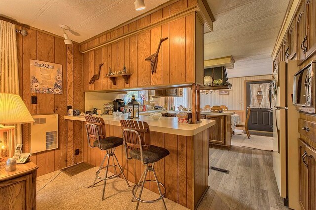 kitchen with wooden walls, kitchen peninsula, a kitchen bar, and light wood-type flooring