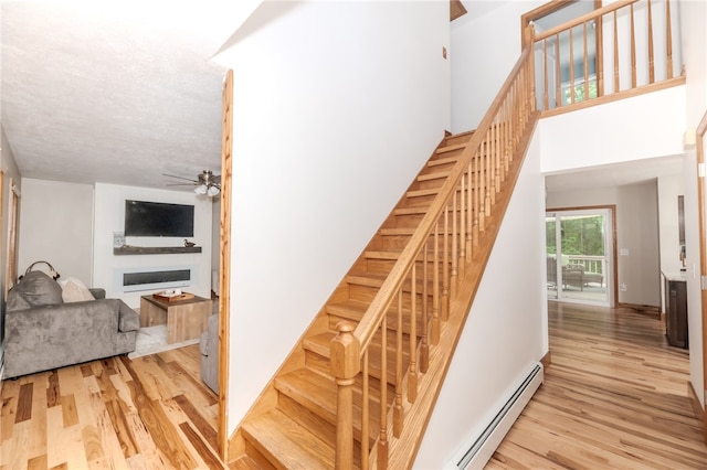 stairway featuring a high ceiling, a textured ceiling, wood-type flooring, ceiling fan, and baseboard heating