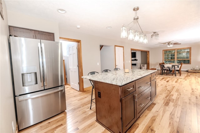 kitchen featuring light wood-type flooring, stainless steel fridge, a kitchen bar, decorative light fixtures, and a center island