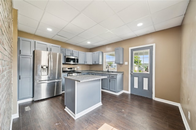 kitchen featuring appliances with stainless steel finishes, a paneled ceiling, gray cabinetry, a kitchen island, and dark wood-type flooring