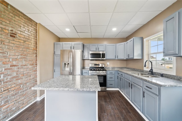 kitchen featuring a paneled ceiling, brick wall, a kitchen island, appliances with stainless steel finishes, and sink