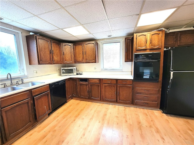 kitchen featuring light wood-type flooring, black appliances, a healthy amount of sunlight, and a drop ceiling