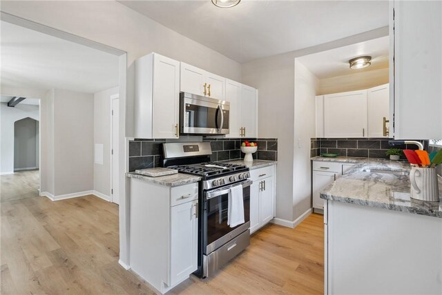 kitchen with white cabinetry, backsplash, appliances with stainless steel finishes, and light hardwood / wood-style floors