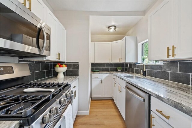 kitchen with decorative backsplash, light hardwood / wood-style flooring, appliances with stainless steel finishes, light stone counters, and sink