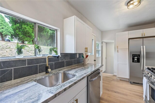 kitchen featuring a wealth of natural light, stainless steel appliances, light stone countertops, and light hardwood / wood-style flooring