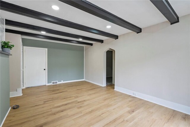 empty room with light hardwood / wood-style floors and beam ceiling