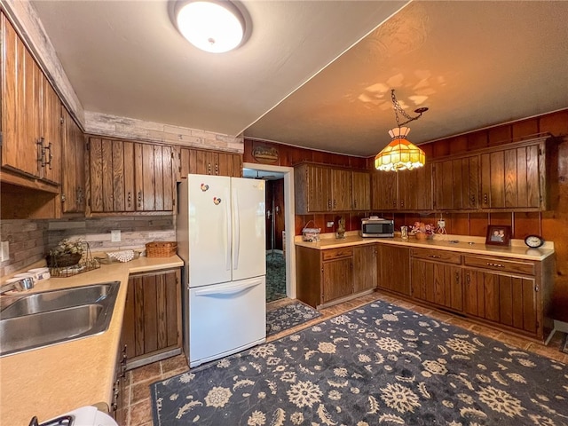 kitchen featuring sink, tasteful backsplash, hanging light fixtures, and white fridge