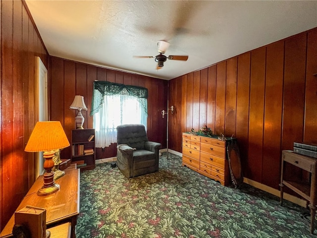 sitting room with carpet flooring, ceiling fan, and wooden walls