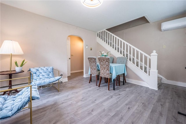 living area with baseboards, arched walkways, a wall unit AC, stairway, and wood finished floors