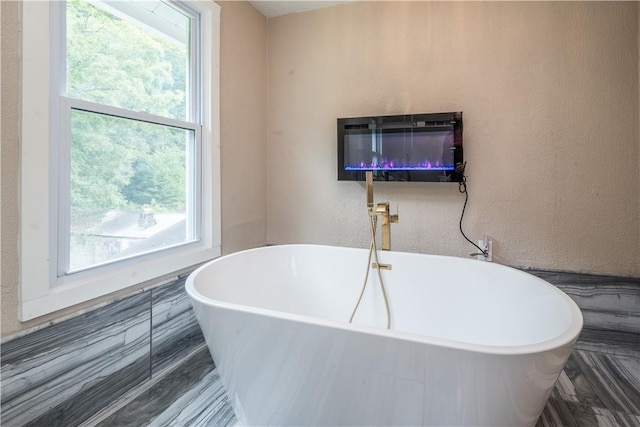 bathroom featuring a glass covered fireplace, a soaking tub, a textured wall, and heating unit