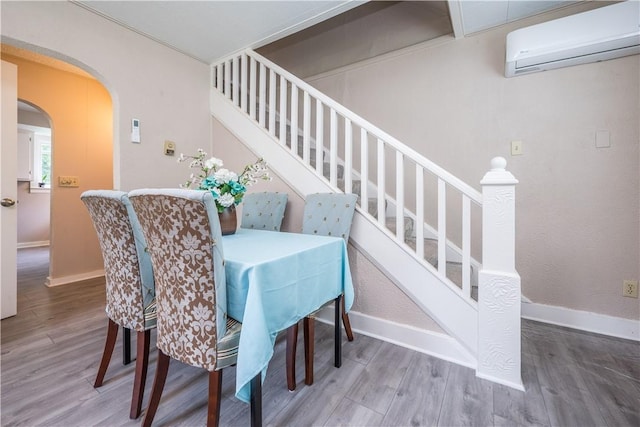 dining space featuring baseboards, arched walkways, wood finished floors, and a wall mounted air conditioner