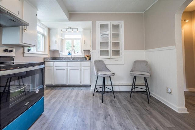 kitchen featuring arched walkways, under cabinet range hood, electric range, white cabinets, and light wood-type flooring