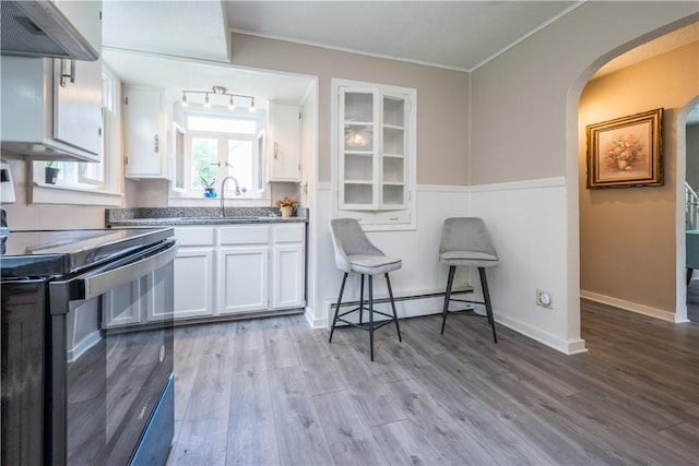 kitchen featuring a baseboard radiator, wall chimney exhaust hood, black range with electric stovetop, white cabinetry, and a sink