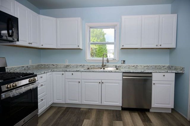 kitchen with dark hardwood / wood-style flooring, white cabinets, light stone counters, sink, and stainless steel appliances