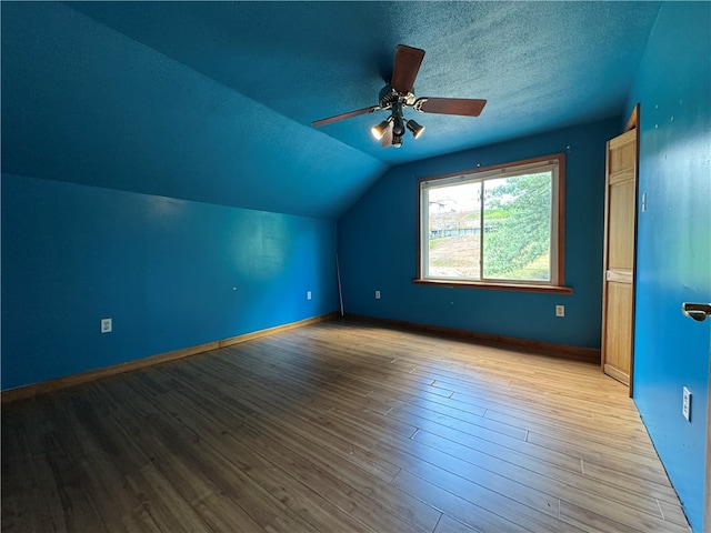 additional living space with ceiling fan, light wood-type flooring, vaulted ceiling, and a textured ceiling