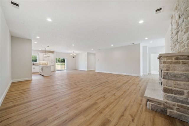 unfurnished living room featuring a stone fireplace, light hardwood / wood-style flooring, and an inviting chandelier