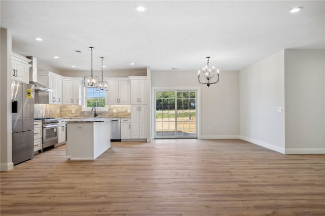 kitchen featuring a kitchen island, wall chimney range hood, a healthy amount of sunlight, and stainless steel appliances