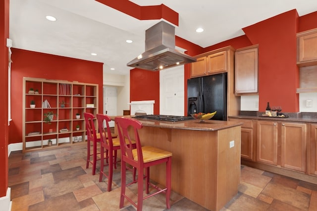 kitchen featuring island range hood, stainless steel gas stovetop, light tile patterned floors, black fridge, and a kitchen island