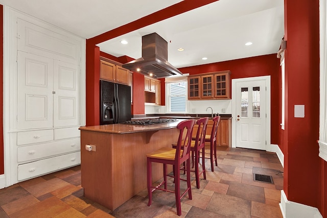 kitchen with black fridge with ice dispenser, a wealth of natural light, dark tile patterned floors, and island range hood