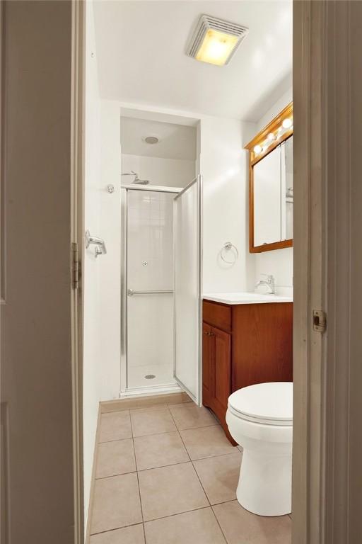 bathroom featuring tile patterned flooring, a shower with door, vanity, and toilet