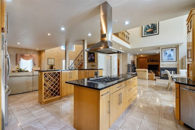 kitchen with dark stone counters, a center island, a tile fireplace, appliances with stainless steel finishes, and island range hood