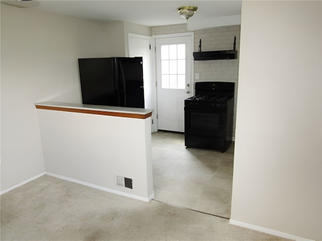 kitchen with brick wall, black appliances, and light colored carpet