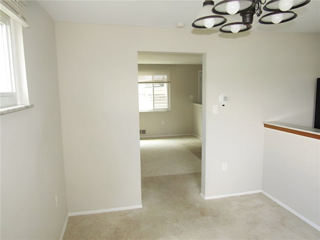 carpeted empty room with an inviting chandelier