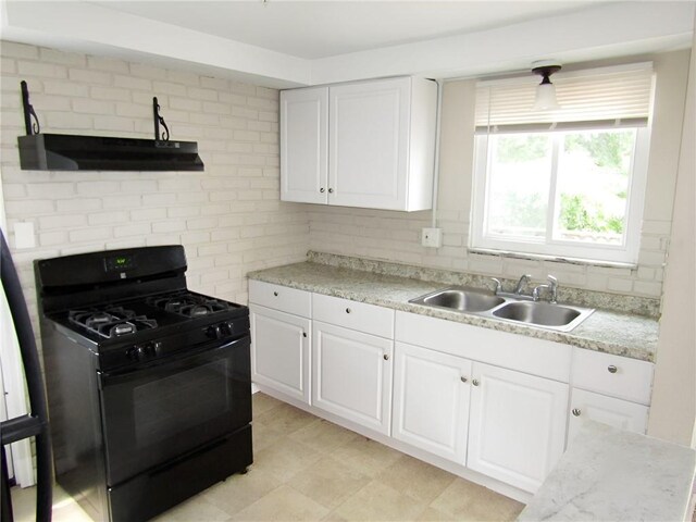 kitchen with sink, light stone countertops, black gas stove, light tile patterned floors, and white cabinets