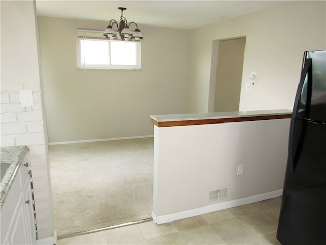 kitchen with decorative light fixtures, black refrigerator, a chandelier, kitchen peninsula, and light colored carpet